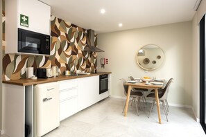 A compact kitchen with a microwave, toaster, and coffee maker on the counter. A dining table with chairs is set for two. - Villa 41 Faro Airport | Studio 2 | 4 Guests | Early/Late Flights (Faro)
