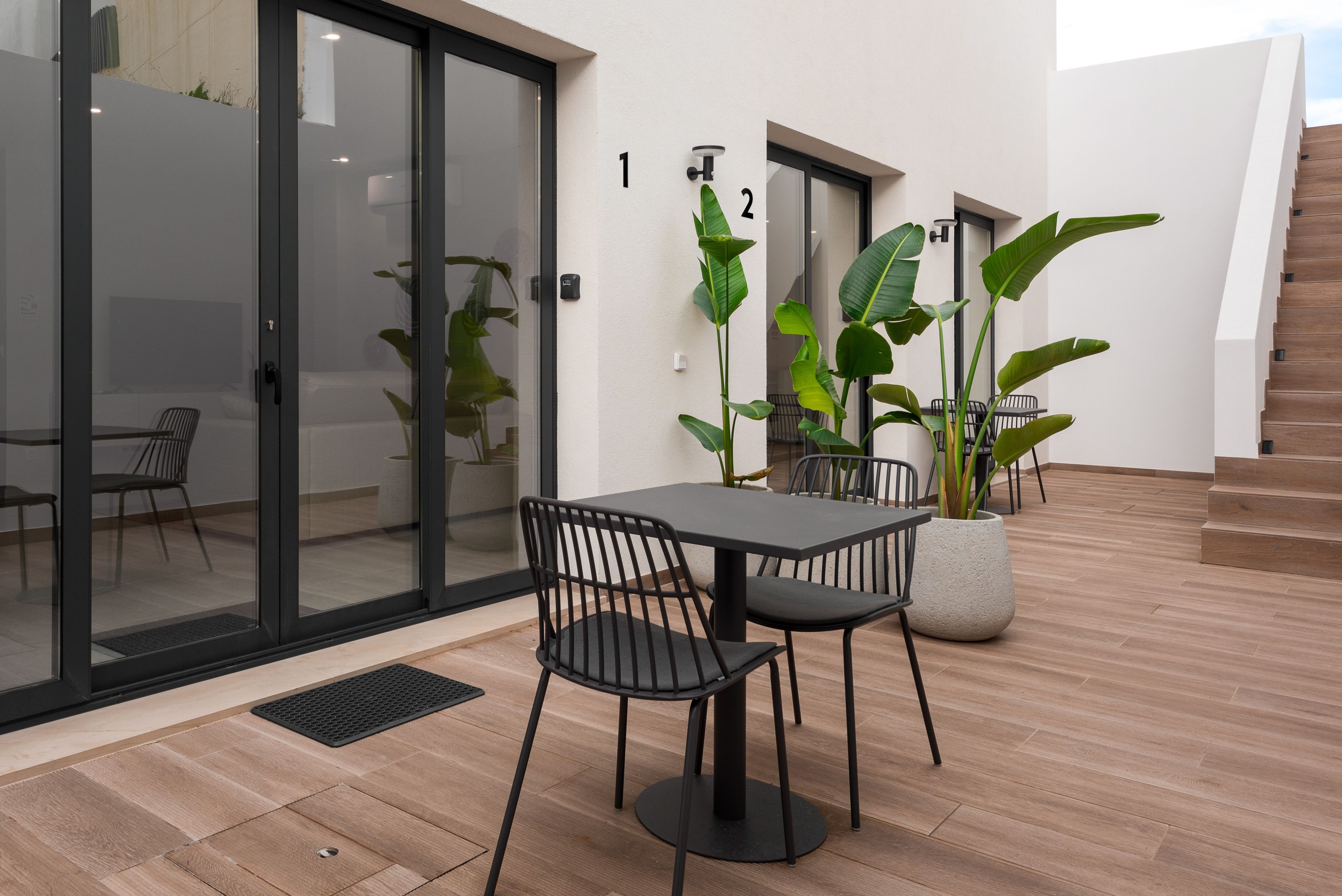 An outdoor patio area with a table and chairs, potted plants, and a staircase.