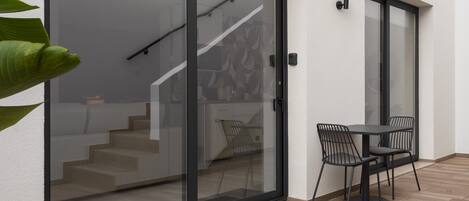 A modern interior with a glass door leading to a staircase, a dining area with a table and chairs, and a wall-mounted light fixture.