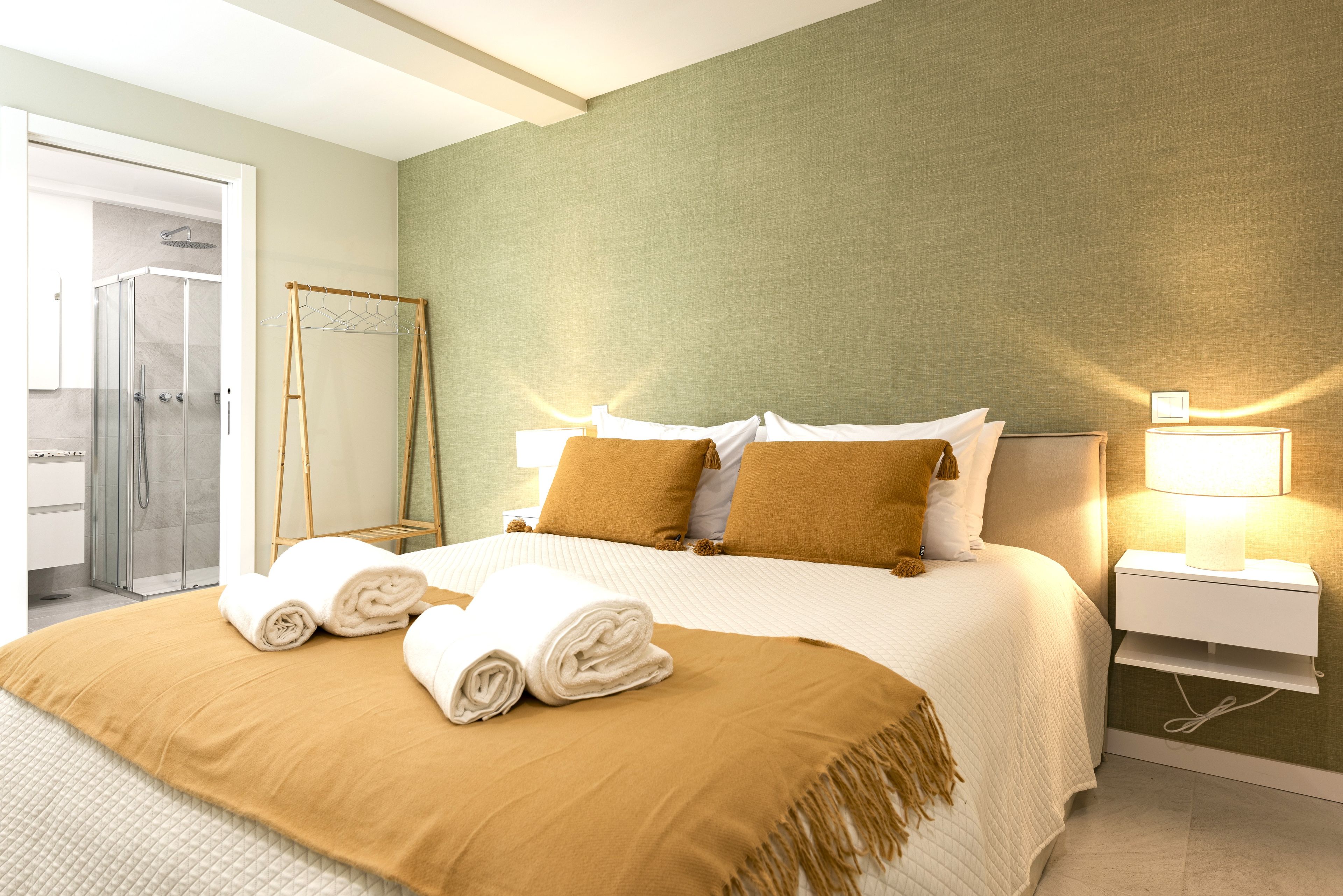 A hotel room with a bed, a nightstand, a lamp, a towel rack, and a shower area.