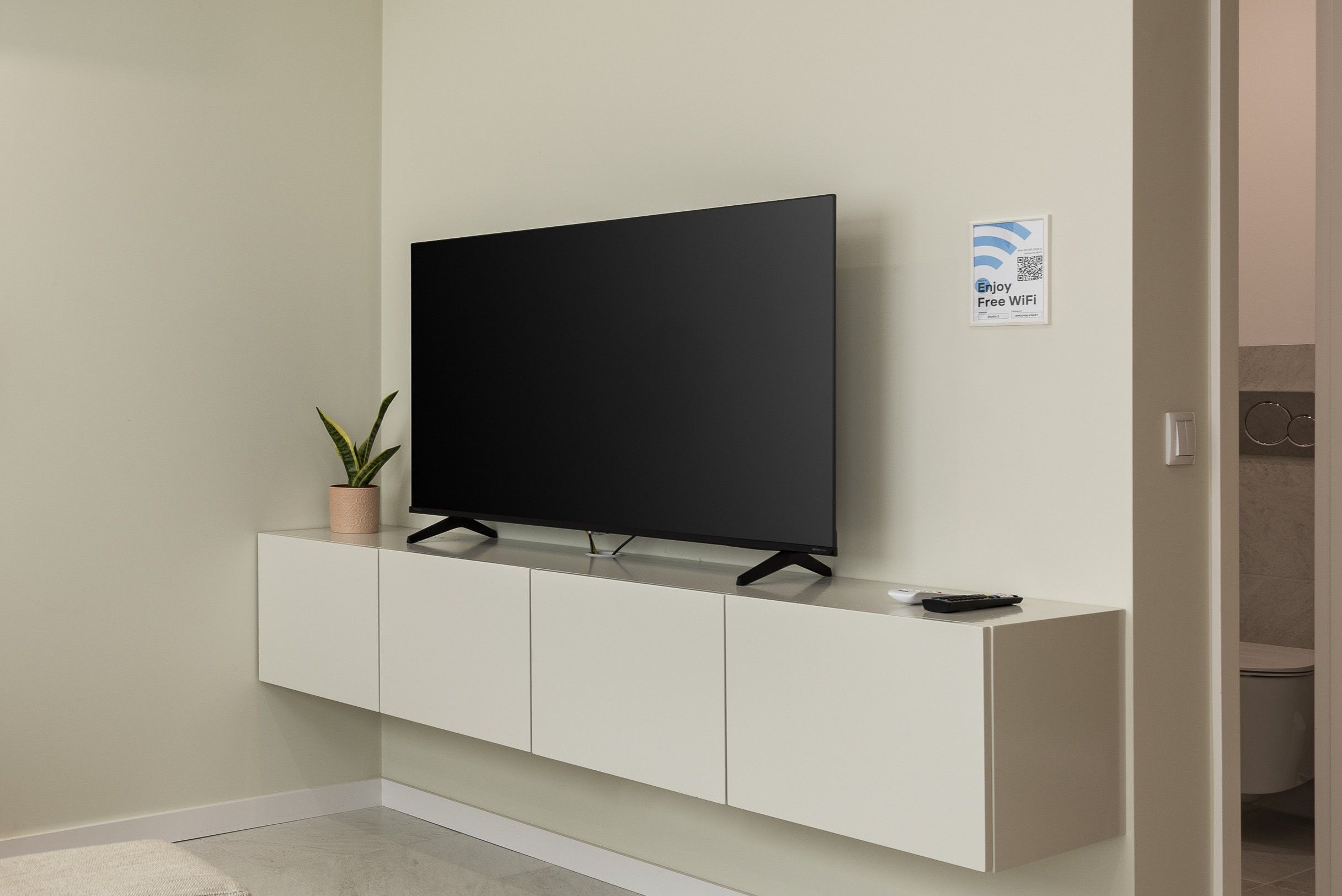 A flat-screen TV mounted on a white cabinet with a potted plant beside it.