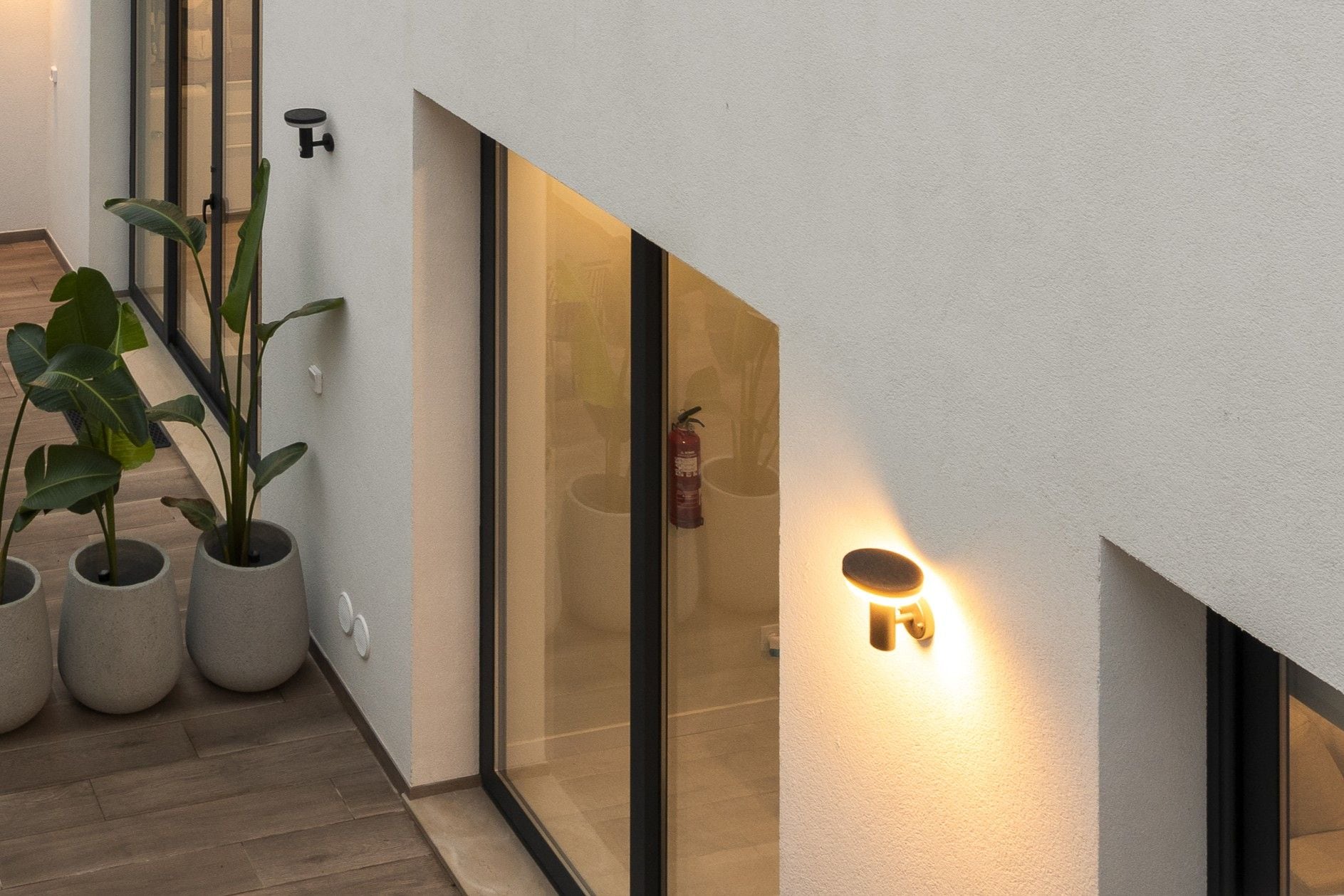 A modern interior with a glass door, potted plants, and a wall-mounted light fixture.