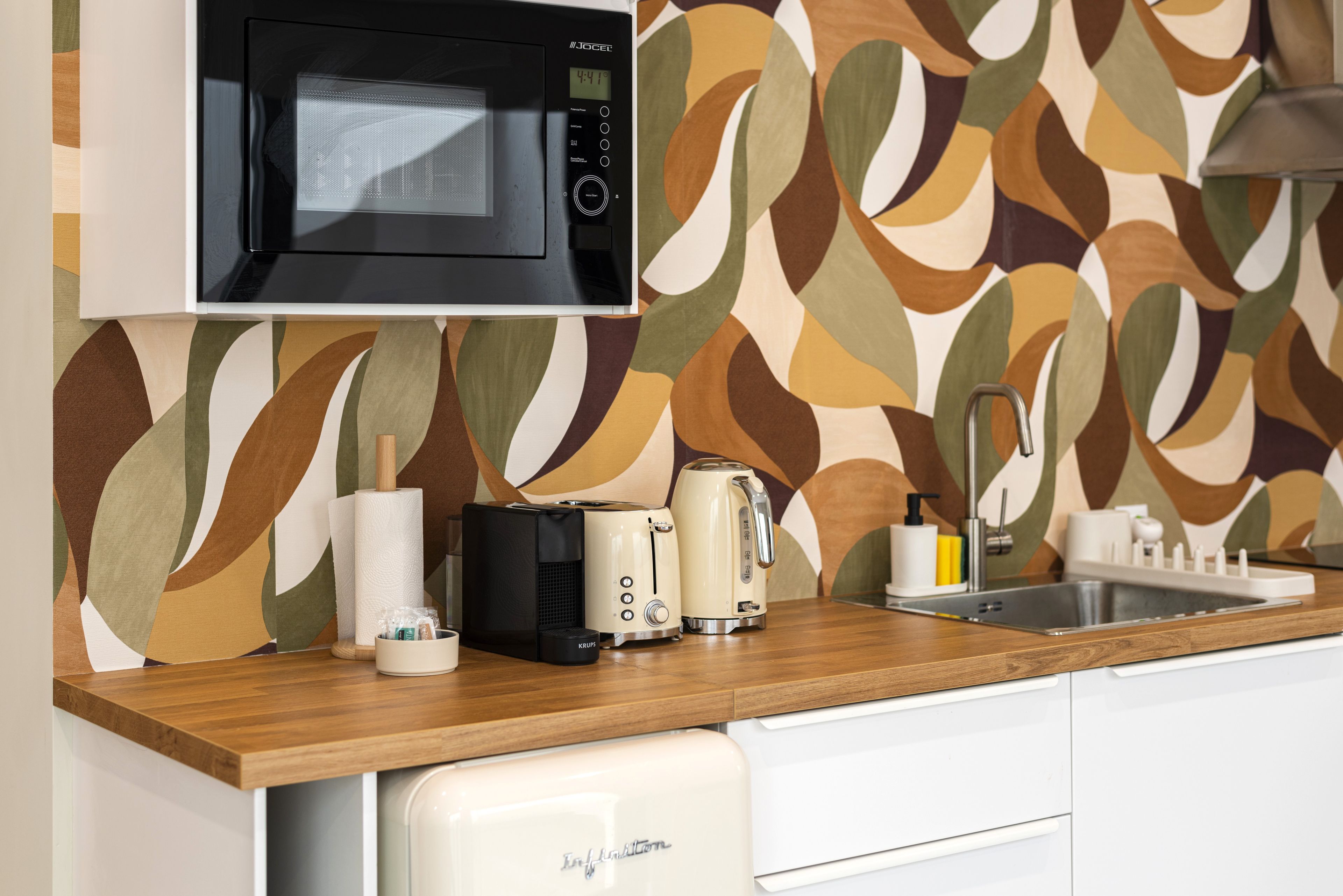 Chic retro kitchenette with espresso maker, toaster, sink, and colorful backsplash.