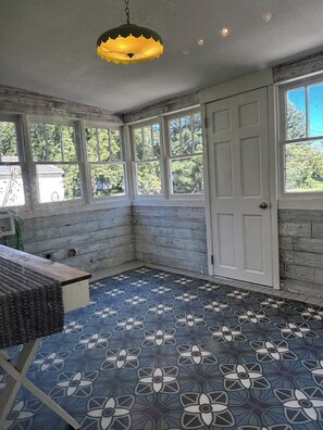 Una habitación con piso estampado, una puerta blanca y un ventanal con vistas a la vegetación.