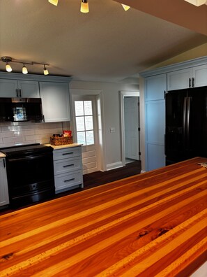 Una cocina con armarios blancos, un refrigerador negro y una encimera de madera.