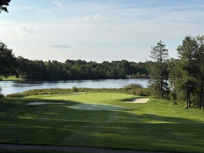 En golfbana med en vattenspegel i bakgrunden, omgiven av träd.