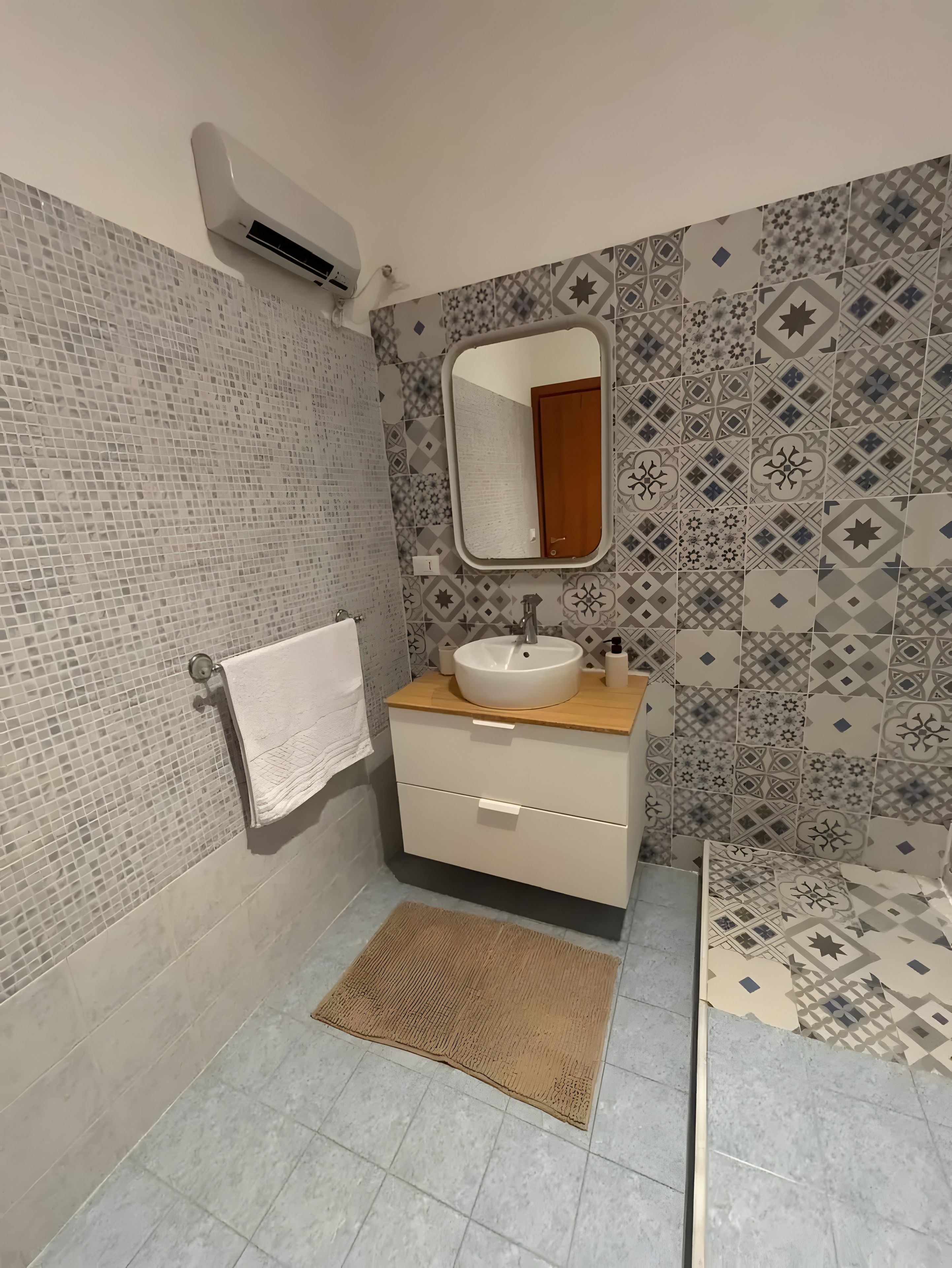 A bathroom with a tiled wall, a sink with a mirror, a towel rack, and a rug.