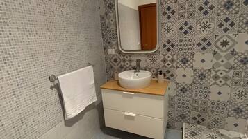 A bathroom with a tiled wall, a sink with a mirror, a towel rack, and a rug.