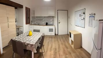 Een kleine keuken met een eethoek, een koelkast en een whiteboard met aantekeningen.