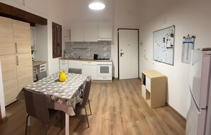 Een kleine keuken met een eethoek, een koelkast en een whiteboard met aantekeningen.