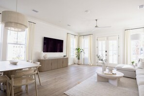 Een ruime woonkamer met een eethoek, een aan de muur bevestigde flatscreen-tv en een plafondventilator.