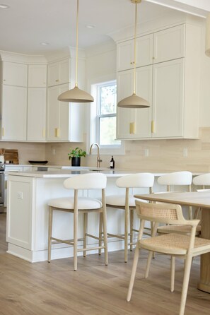 A kitchen with white cabinets, a central island with bar stools, pendant lighting, and a window. - NEW! Spacious Home, 3rd Fl Patio and Bar w/ Costal View! (Panama City)