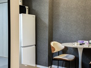 Eine kompakte Küche mit einem weißen Kühlschrank, einem runden Tisch mit einem Stuhl und einer kleinen Arbeitsfläche.