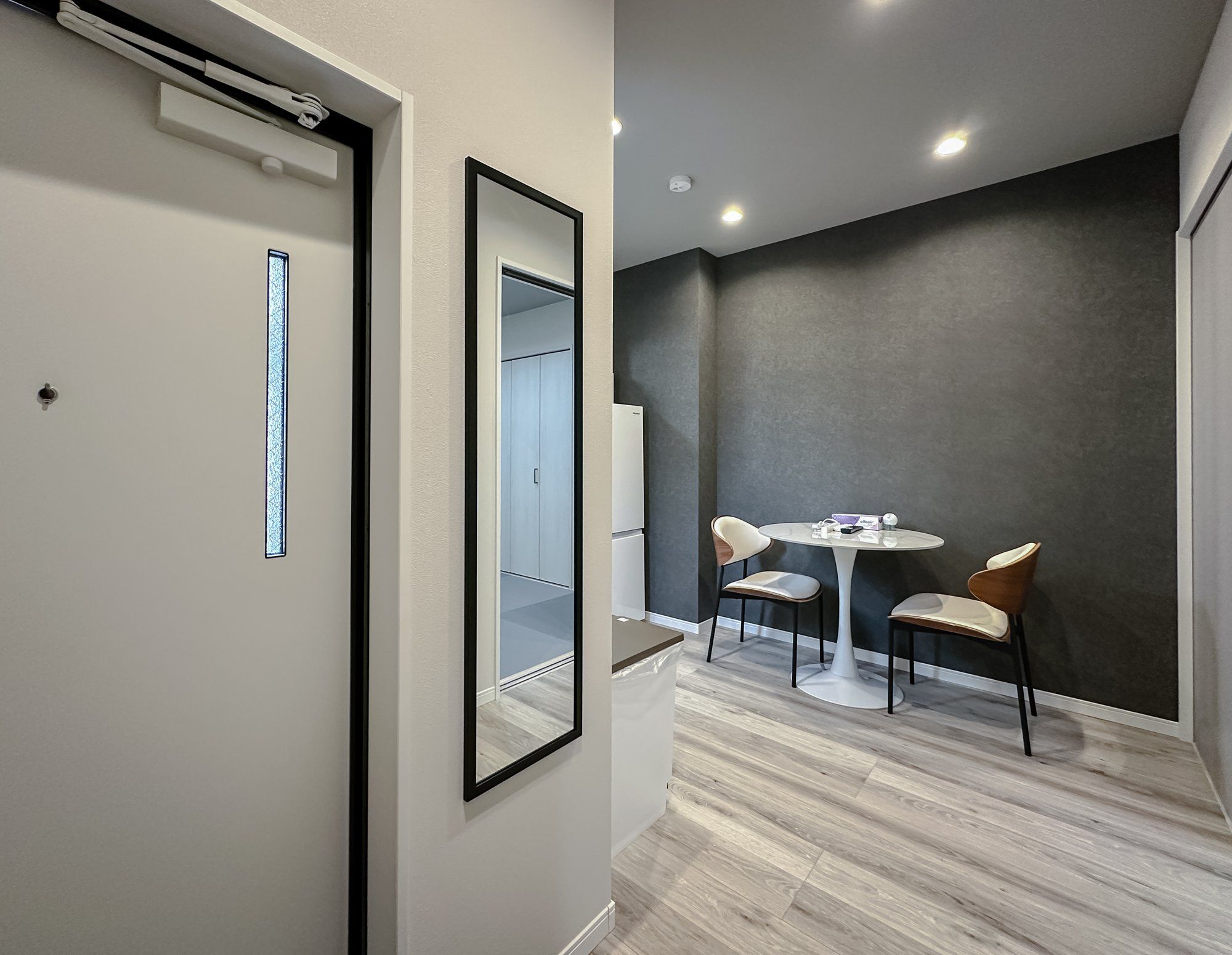 Een moderne kamer met een grote spiegel, een klein tafeltje met stoelen en een grijze accentmuur.