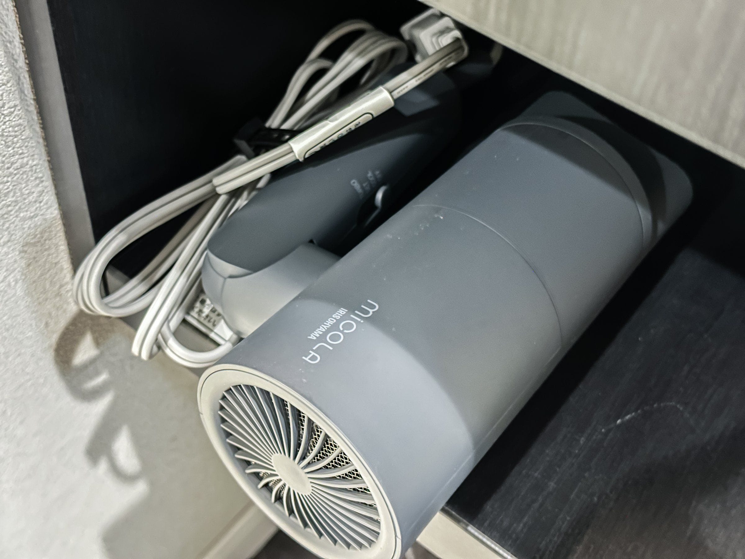 Um dispositivo cilíndrico cinzento com uma abertura de ventilação, um cabo e uma etiqueta com a inscrição 'MICOOLA IRIS BRAVA'.