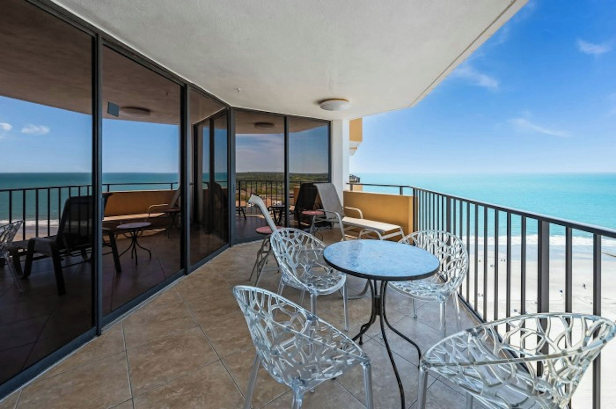 A balcony with a glass railing overlooking the sea, furnished with chairs and a table.