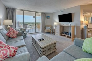 A modern living room with a sofa, a coffee table, and a television. - Maisons-Sur-Mer 1602 Ocean View 2BR- Outdoor Pool (Myrtle Beach)