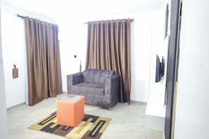 Ein Wohnzimmer mit einem grauen Sofa, einem kleinen orangefarbenen Hocker und einem gemusterten Teppich.
