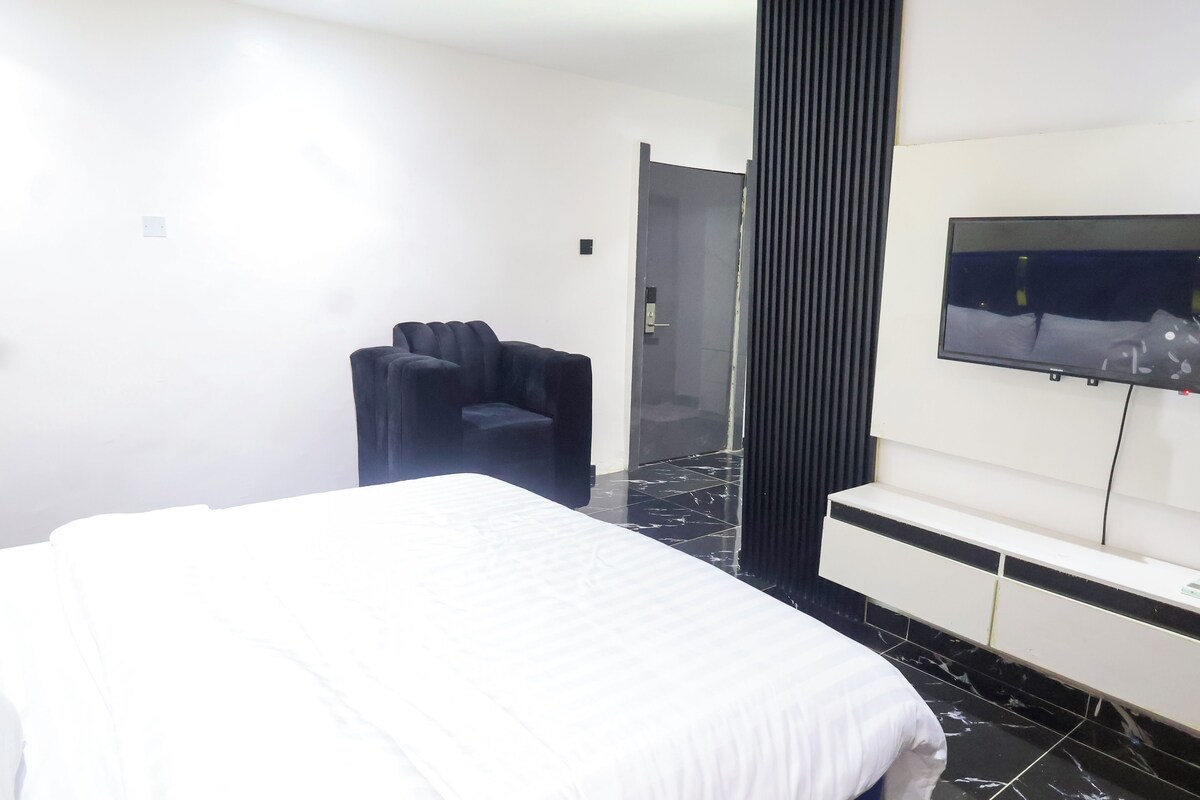 Ein Hotelzimmer mit einem Bett, einem schwarzen Sessel, einem Fernseher und einer Tür.