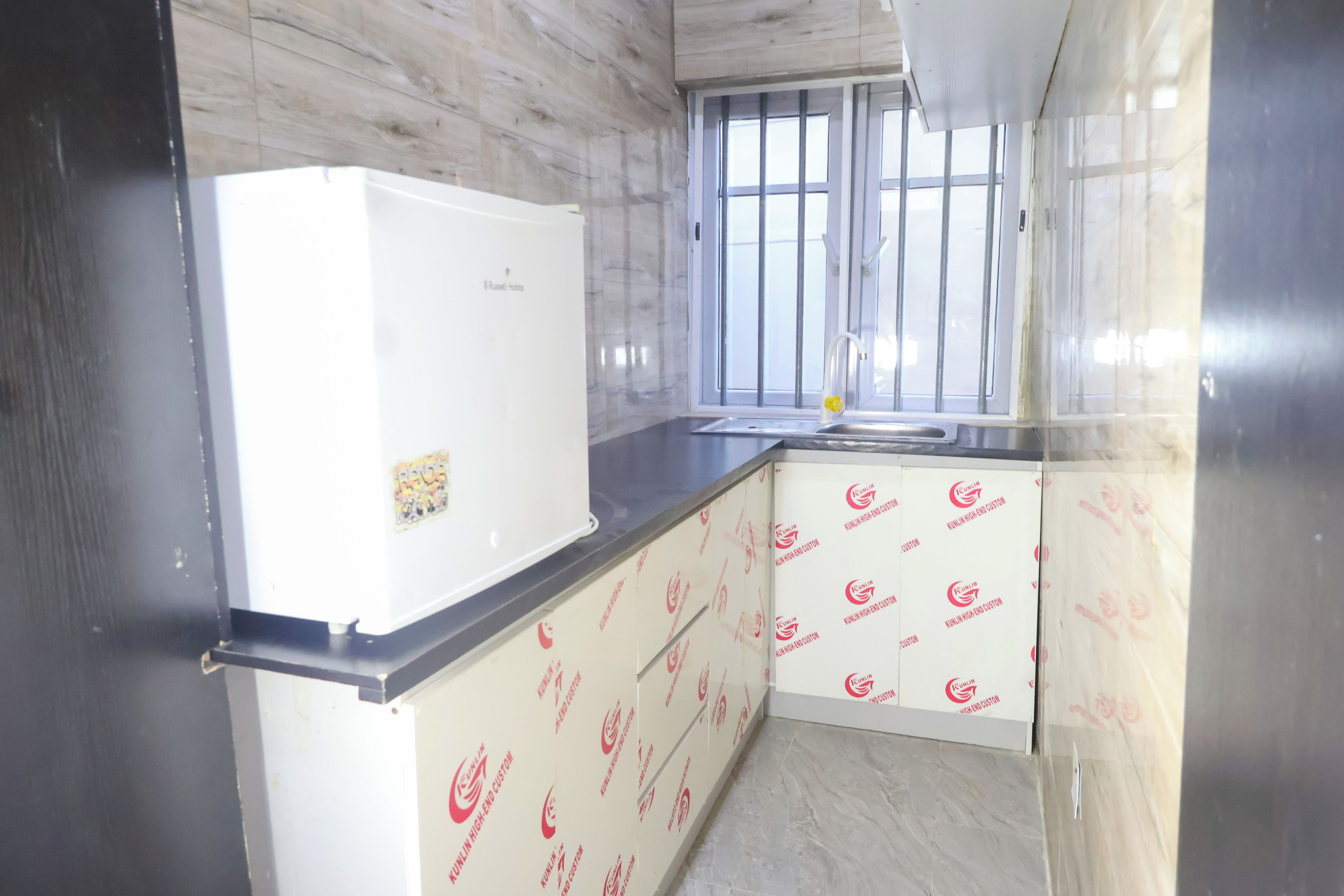 Cocina compacta con refrigerador blanco, una ventana con rejas y revestimientos de pared estampados.