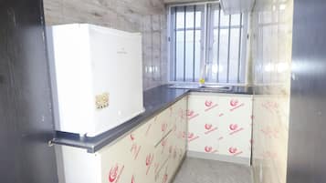 A compact kitchen with a white refrigerator, a window with metal bars, and patterned wall coverings.