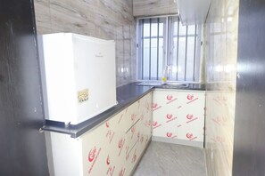 Eine kleine Küche mit einem weißen Kühlschrank, einem Fenster mit Metallgitter und Wandverkleidungen mit Muster.