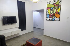 A modern interior with a flat-screen TV mounted on the wall, a large abstract painting, and a small orange table.