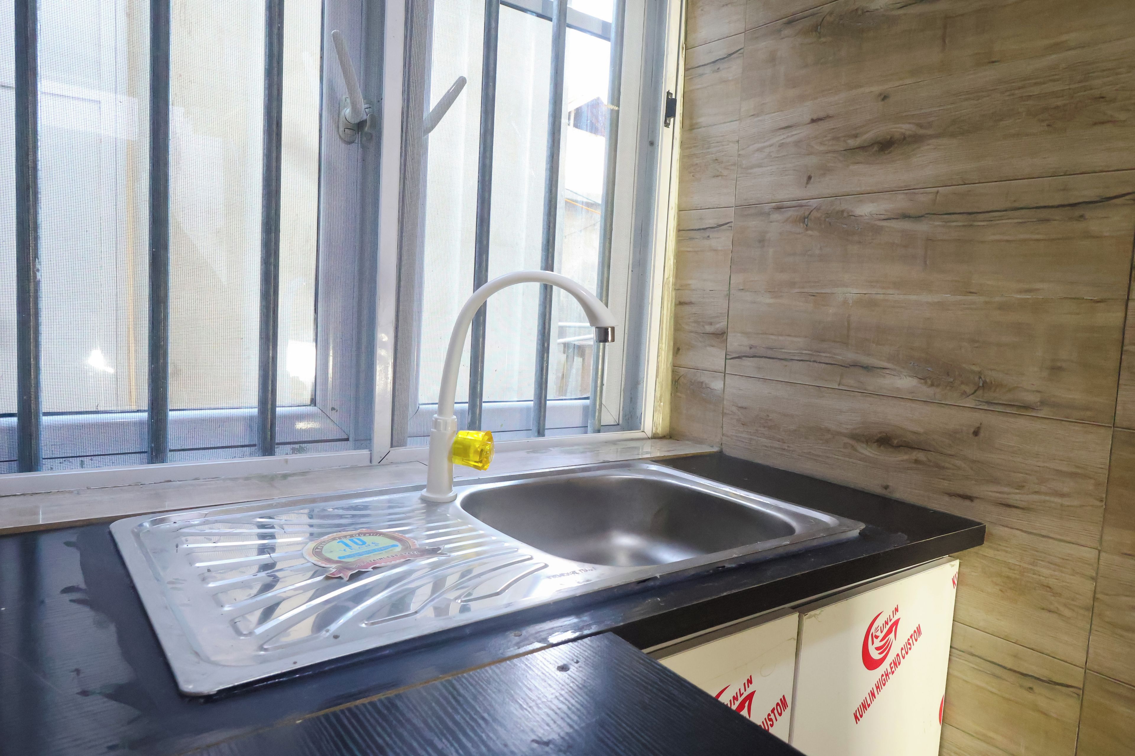 Una cocina con un lavamanos de acero inoxidable, una ventana con mosquitero y armarios de madera.