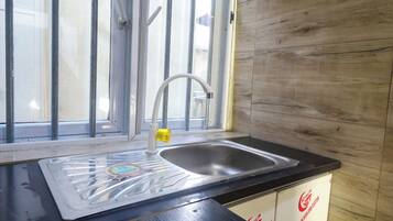Una cocina con un lavamanos de acero inoxidable, una ventana con mosquitero y armarios de madera.