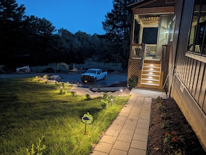 Un camino de entrada que lleva a una casa de madera con garaje, una camioneta estacionada cerca y un sendero bien iluminado.