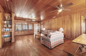 A wooden-paneled room with a sofa, a table, and a bookshelf. - Rustic Eight Bedroom Beach House Steps from the Ocean (North Myrtle Beach)