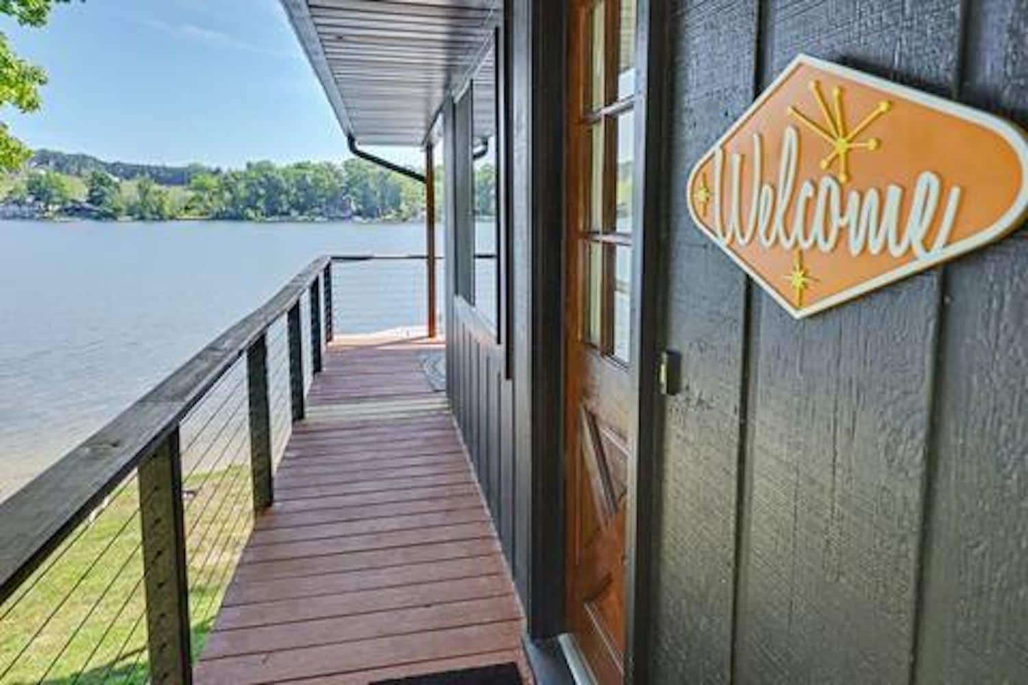 A wooden deck leading to a building with a 'Welcome' sign, overlooking a body of water.