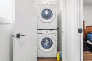 A laundry room with two stacked washing machines, a door, and a small yellow object on the floor. - 3BR Spacious Home • Mins to UofA, Whyte & Downtown (Edmonton)