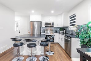 A modern kitchen with stainless steel appliances, a black countertop, and bar stools. - 3BR Spacious Home • Mins to UofA, Whyte & Downtown (Edmonton)