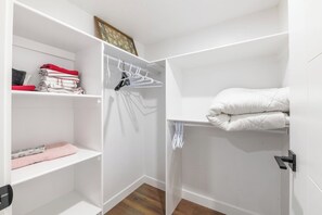 A white closet with shelves, a hanging rod, and a bed with white bedding. - 3BR Spacious Home • Mins to UofA, Whyte & Downtown (Edmonton)