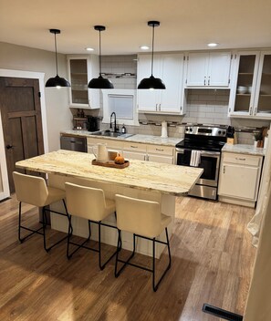 Una cocina moderna con una isla grande, luces colgantes y piso de madera.