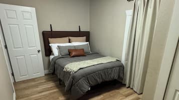 Una camera da letto con un letto, una porta, una finestra con tende e una lampada a soffitto.
