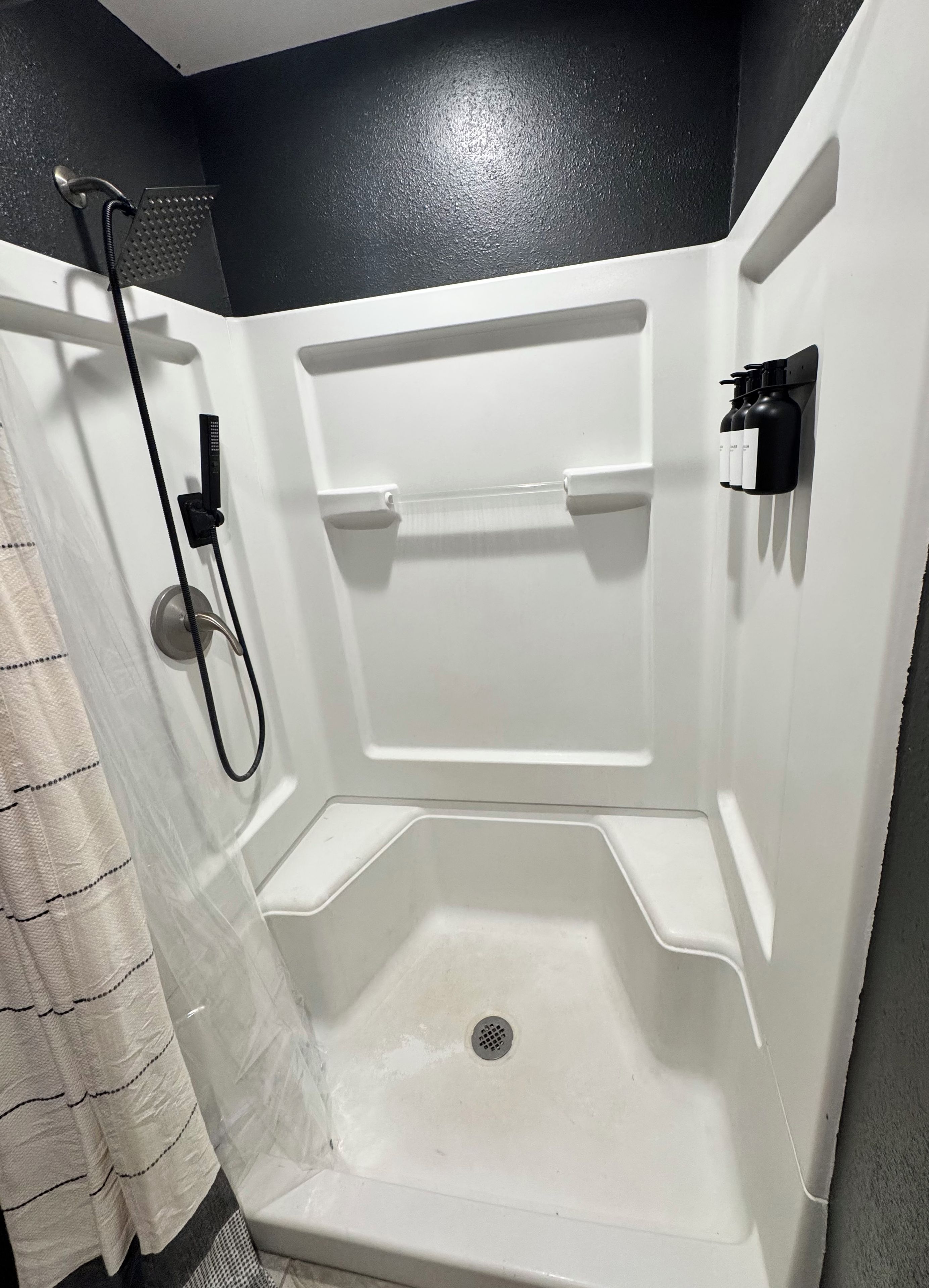 Une cabine de douche équipée d’un pommeau de douche à main, d’un distributeur de savon mural et d’un porte-serviettes.