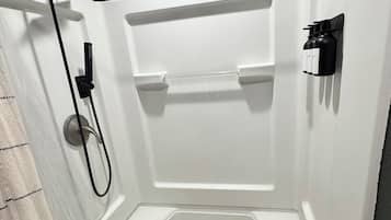 Une cabine de douche équipée d’un pommeau de douche à main, d’un distributeur de savon mural et d’un porte-serviettes.