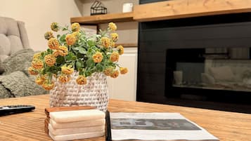 Un tavolo di legno con un cesto intrecciato contenente fiori gialli, un telecomando e una rivista.