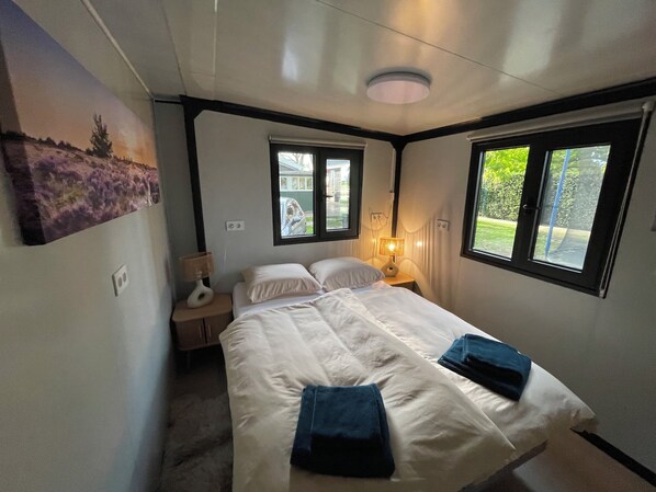 A bedroom with a bed, two bedside lamps, a window, and a wall-mounted painting. - Knus chalet met privé jacuzzi tussen Hoorn en Enkhuizen (Wijdenes)