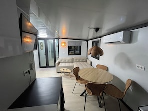A modern interior with a sofa, round table, and wicker chairs. - Knus chalet met privé jacuzzi tussen Hoorn en Enkhuizen (Wijdenes)