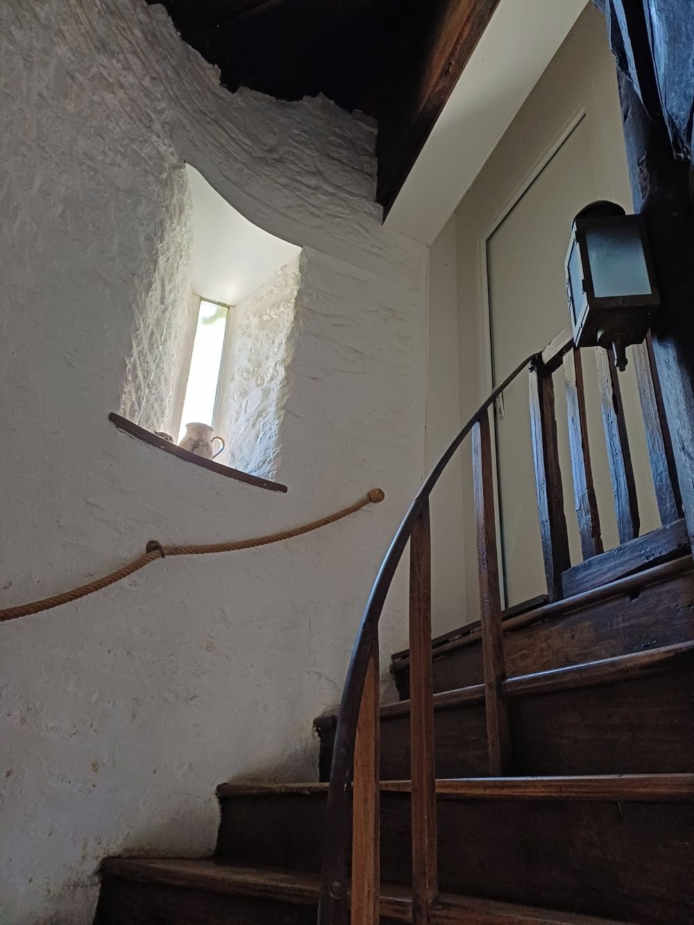 Una escalera de madera con barandilla, que lleva a una puerta con un ventanal encima.