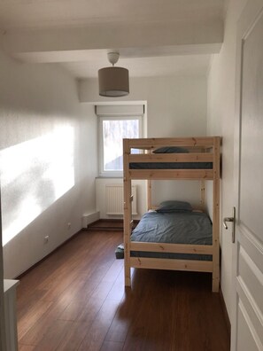 Een stapelbed in een kamer met een raam, een radiator en een deur.