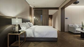 Una habitación de hotel moderna con una cama grande, mesita de noche, lámpara y una zona de estar con sofá y una pequeña mesa.