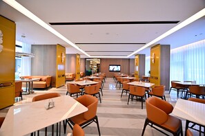 Een moderne eetruimte met meerdere tafels en stoelen, een televisiescherm en een bar op de achtergrond.