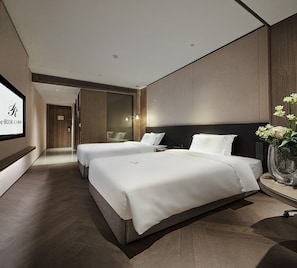 A modern hotel room with two beds, a large mirror, and a potted plant.