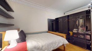 A bedroom with a bed, a bedside table with a lamp, a wardrobe with hanging clothes, and a mirror. - Stunning Studio Flat, Charring Cross Prime Location of London (London)