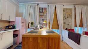 A kitchen with a central island, white cabinets, a pink refrigerator, and a dining area with a bench and curtains. - Stunning Studio Flat, Charring Cross Prime Location of London (London)