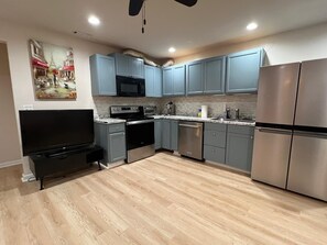 A modern kitchen with grey cabinets, stainless steel appliances, a flat-screen TV, and a wooden floor. - Private 2BR Guest Suite, No Stairs, Garage (Woodstock)